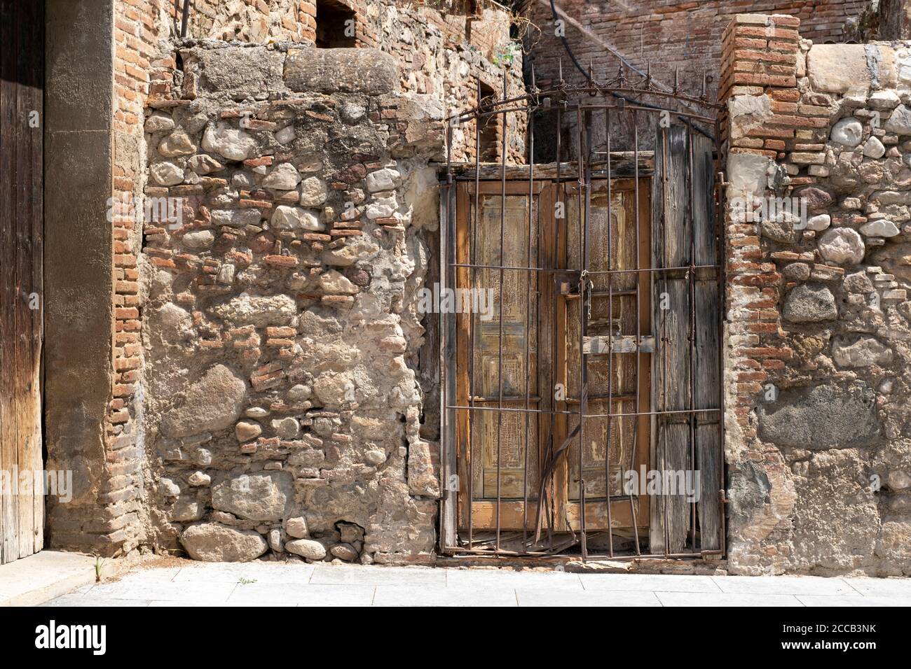 Stone wall in a rural building and a damaged old wooden door. Travel destination background in Spain, Mediterranean and South Europe country. Stock Photo