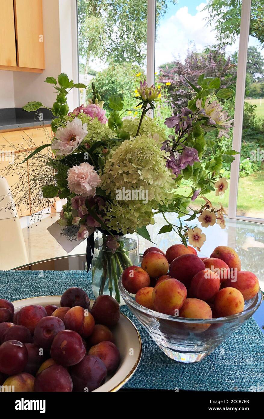Dark red dessert plums and Victoria plums  in a still life with florist's posy of garden flowers Stock Photo