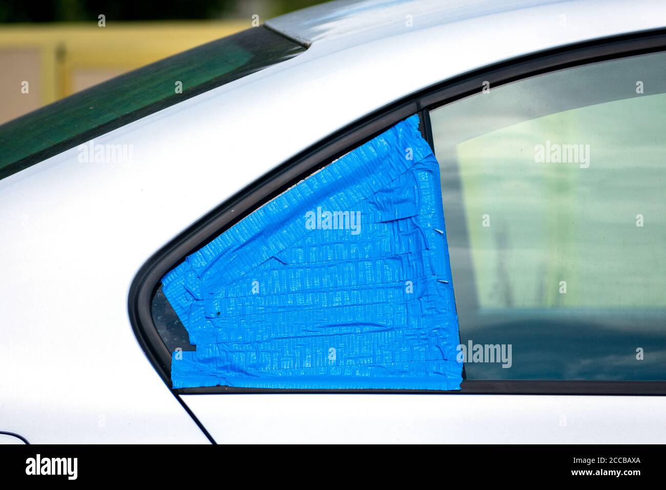 Broken and damaged car window temporarily covered with blue tape to protect interior from rain and water. Smash-and-grab automobile break-ins. Stock Photo