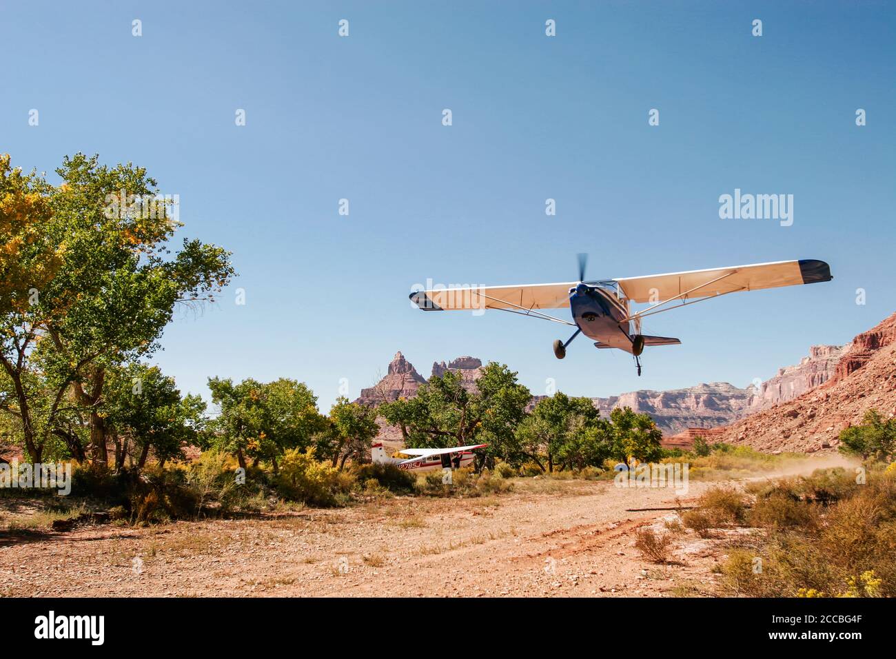 A experimental kit plane takes off from  the remote Mexican Mountain airstrip on the San Rafael Swell in Utah.  A Cessna 185 Skywagon is parked by the Stock Photo