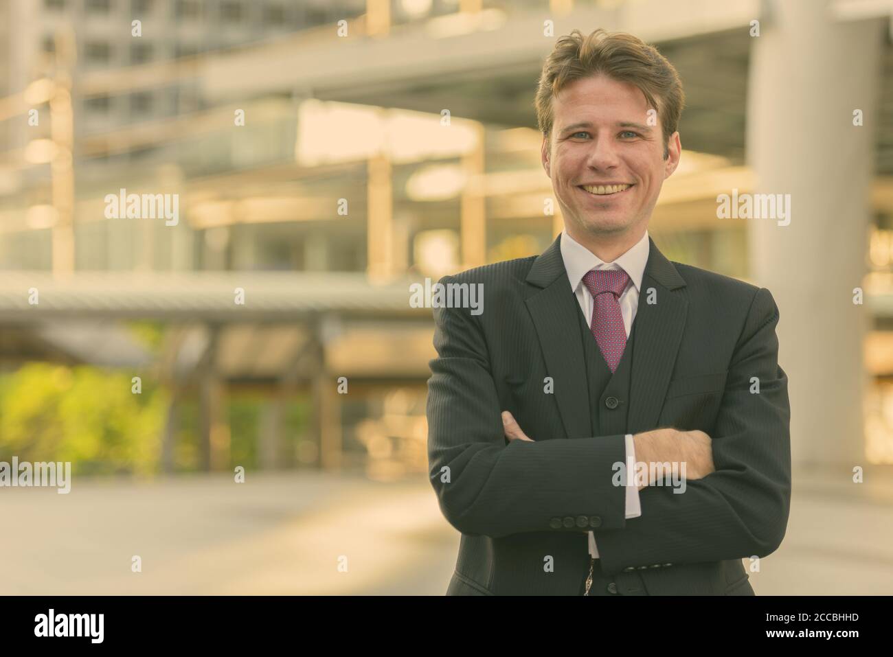 Happy businessman smiling with arms crossed in front of modern building ...