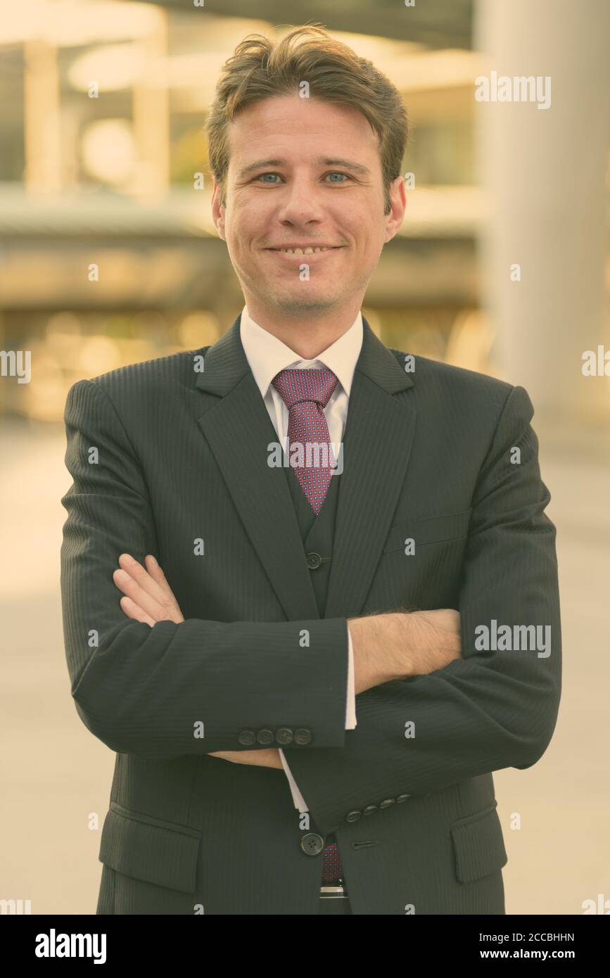 Happy businessman smiling with arms crossed in front of modern building ...