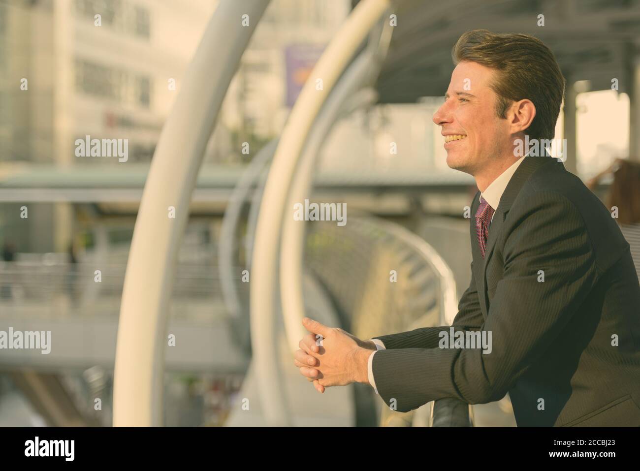 Profile view of happy businessman smiling and thinking in footbridge at ...