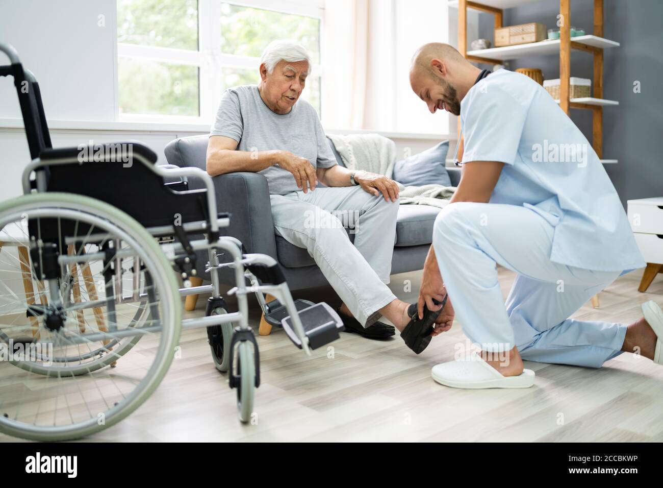 Old Senior Home Care. Nurse Helping Patient To Dress Shoes Stock Photo