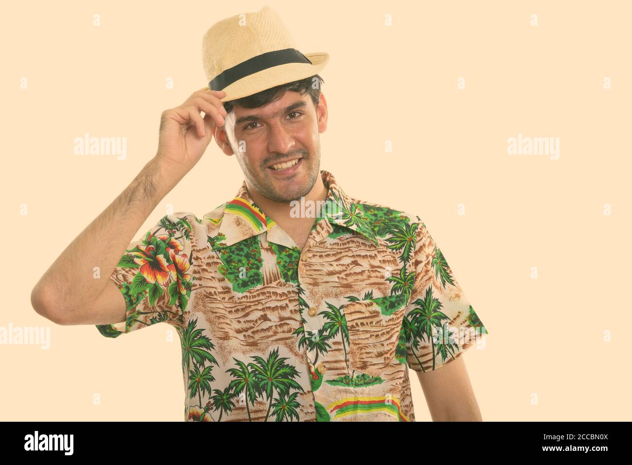 Studio shot of young happy Persian man smiling while holding hat Stock ...