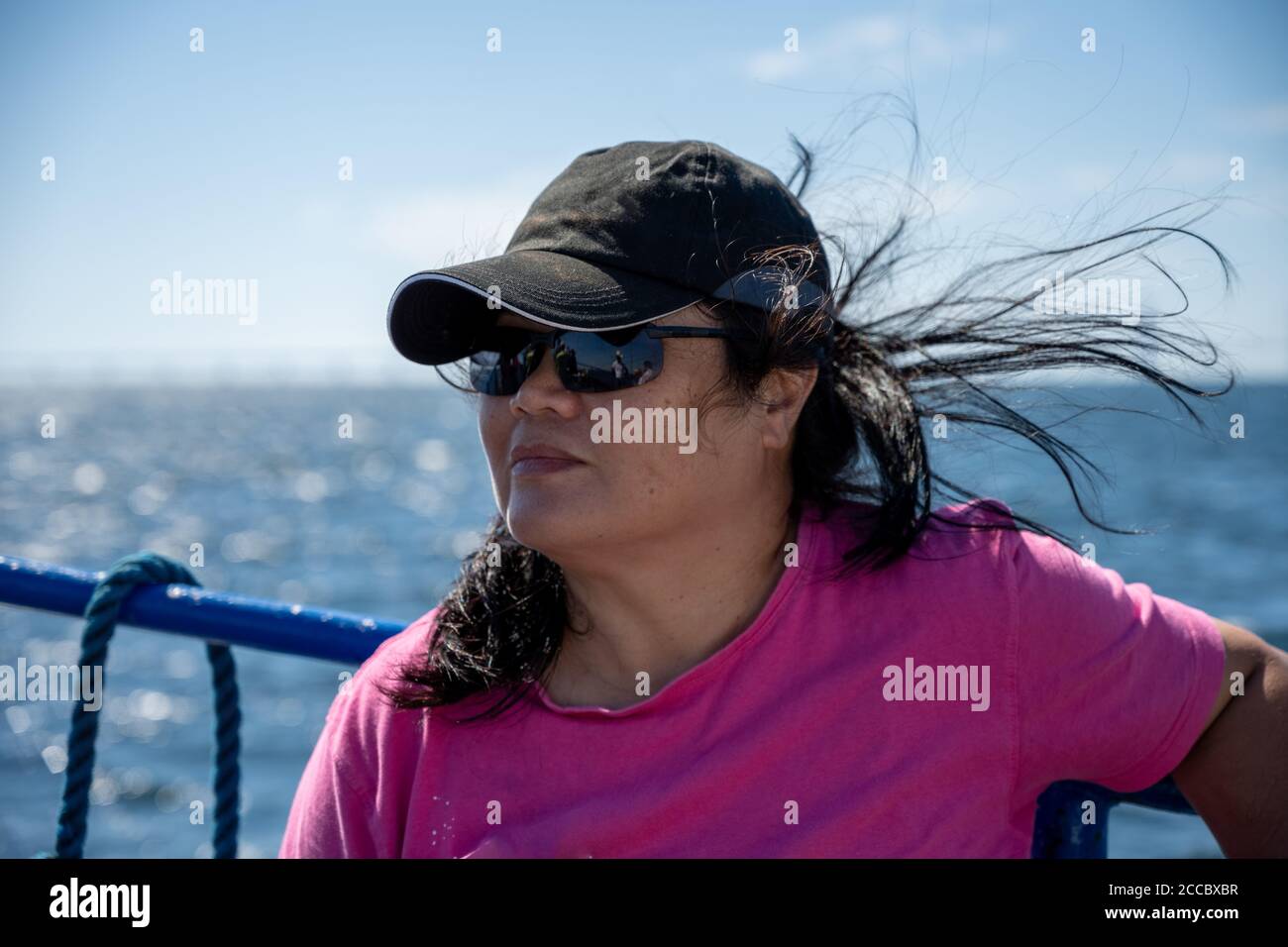 A middle-aged Asian woman on a boat trip a hot summer day on the ocean outside Malmo, Sweden. Bright blue sky and ocean in the background Stock Photo