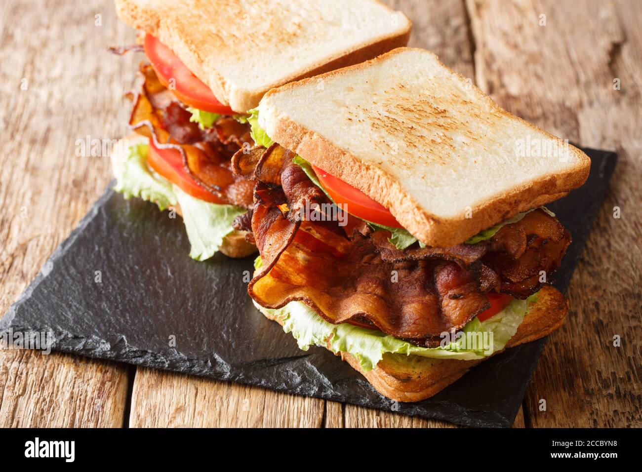 American fast food blt sandwich with bacon, fresh salad and tomatoes close-up on a slate board on the table. horizontal Stock Photo