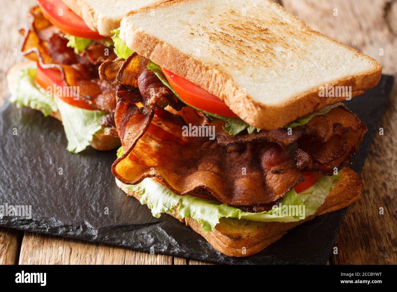 Popular American appetizer blt sandwiches with crispy bacon, fresh salad and tomatoes close-up on a slate board on the table. horizontal Stock Photo