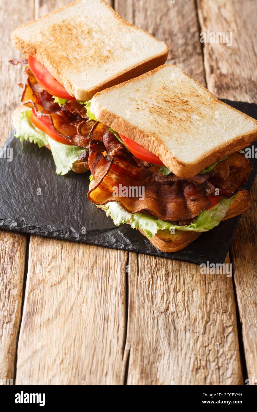 Homemade sandwiches with crispy bacon, fresh salad and tomatoes close-up on a slate board on the table. vertical Stock Photo