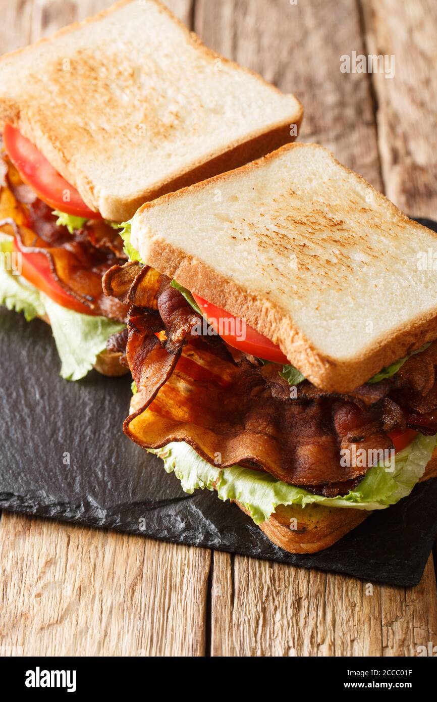 Classic blt toasted bread sandwich with crispy bacon, fresh iceberg lettuce and tomatoes close-up on a slate board on the table. vertical Stock Photo