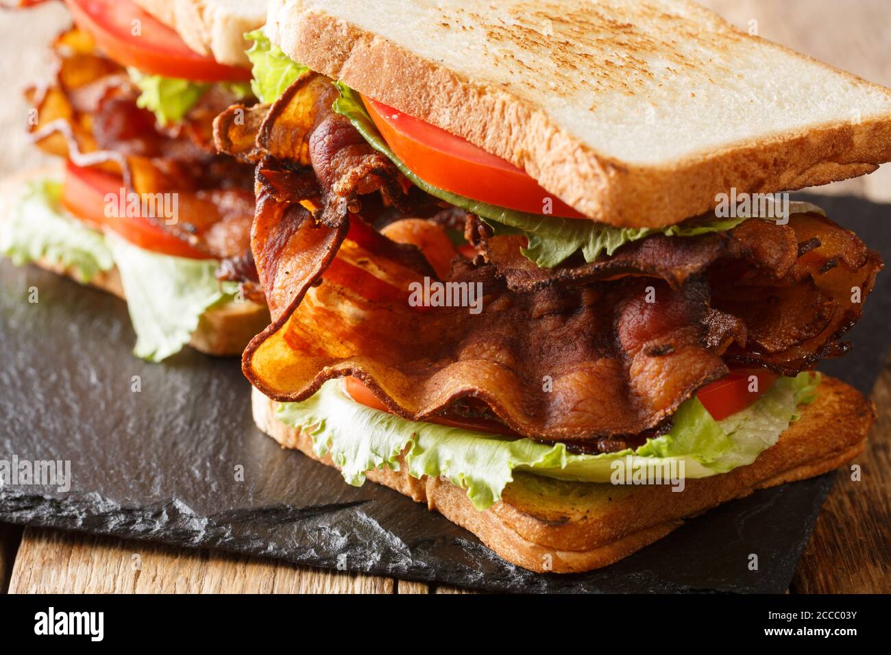 blt sandwich with crispy bacon, fresh iceberg salad and tomatoes close-up on a slate board on the table. horizontal Stock Photo