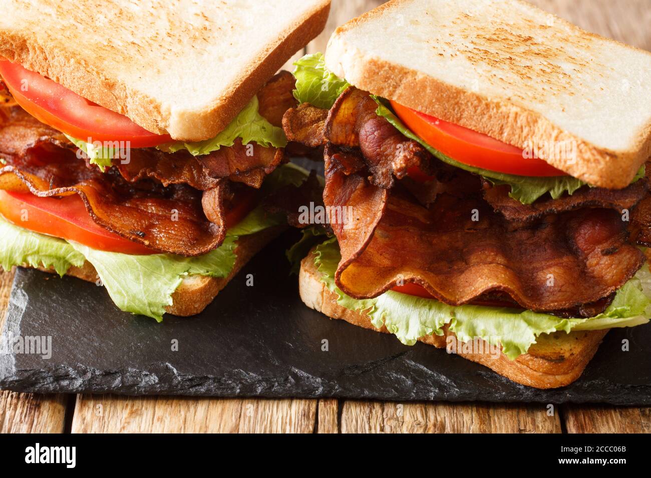 Traditional American blt sandwich with bacon, iceberg lettuce and tomatoes close-up on a slate board on the table. horizontal Stock Photo