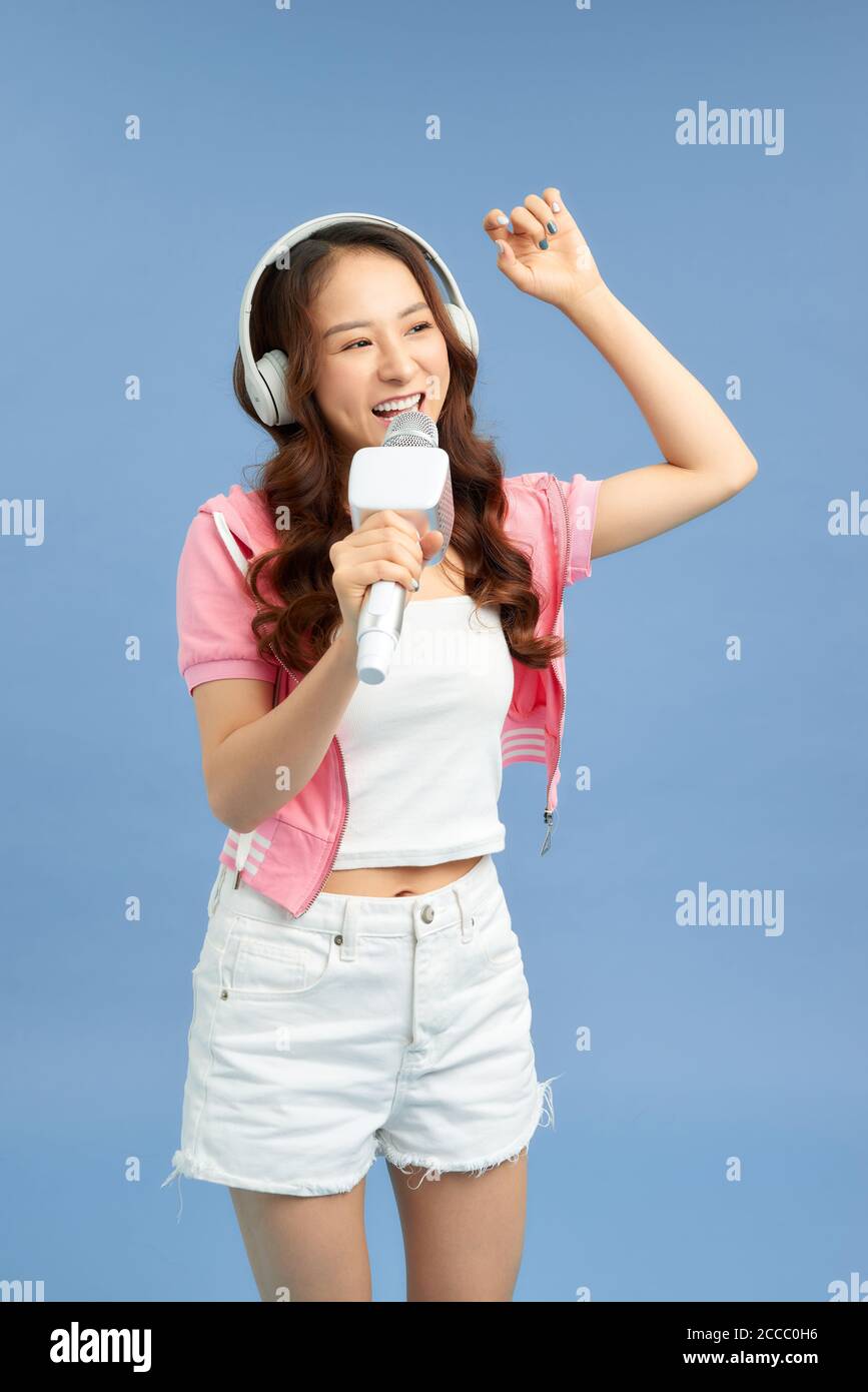 Beautiful Asian girl with microphone sings and headphone isolated over blue background. Stock Photo