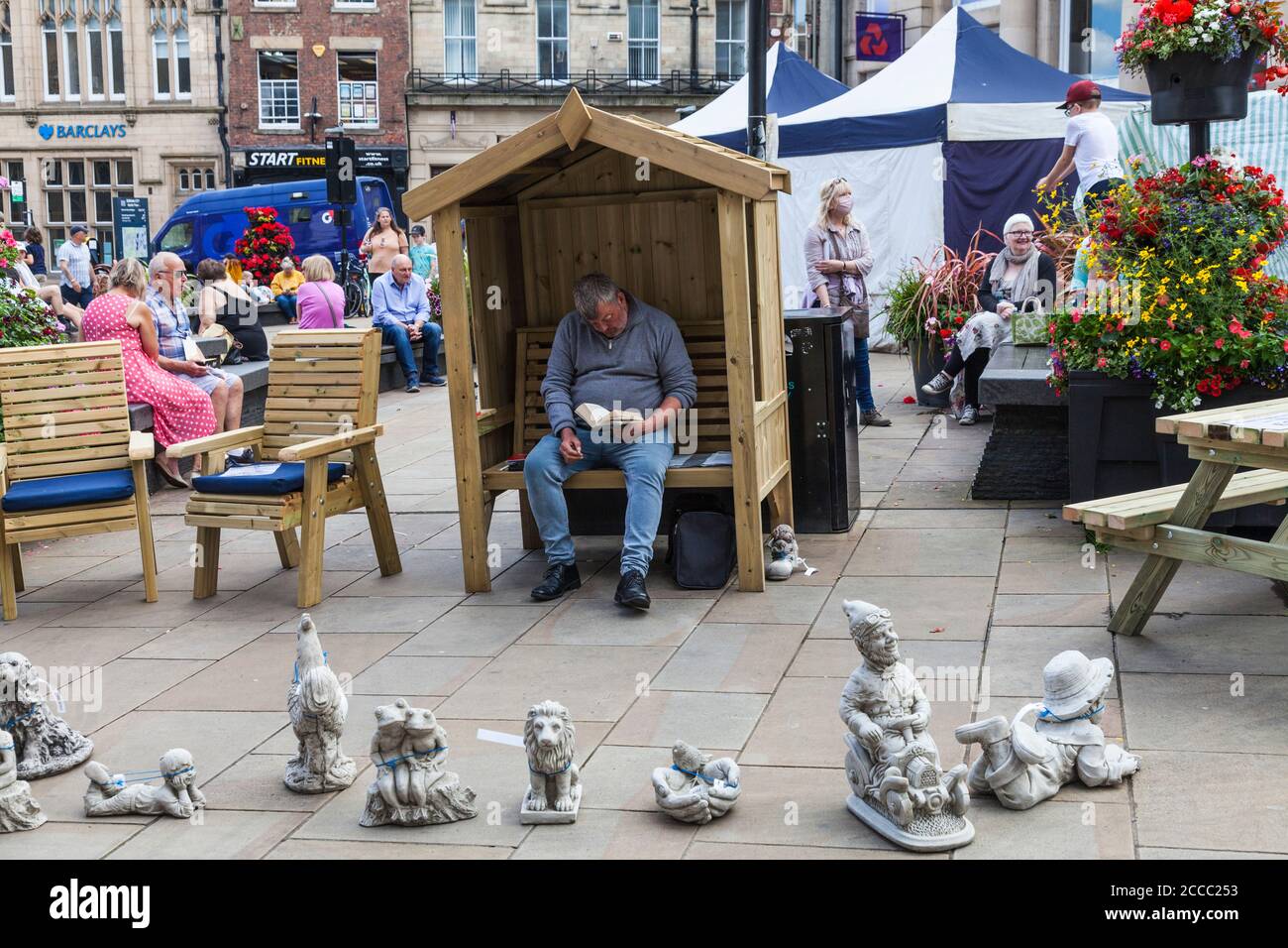 Durham city centre on a market day in north east England.A white male trader sat reading a book surrounded by his craftware Stock Photo