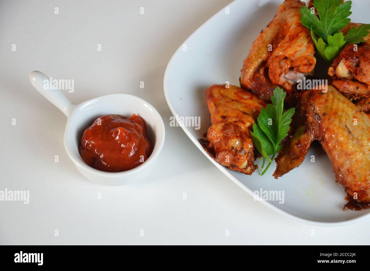 plate of chicken wings on white table red sauce in a gravy boat Stock Photo