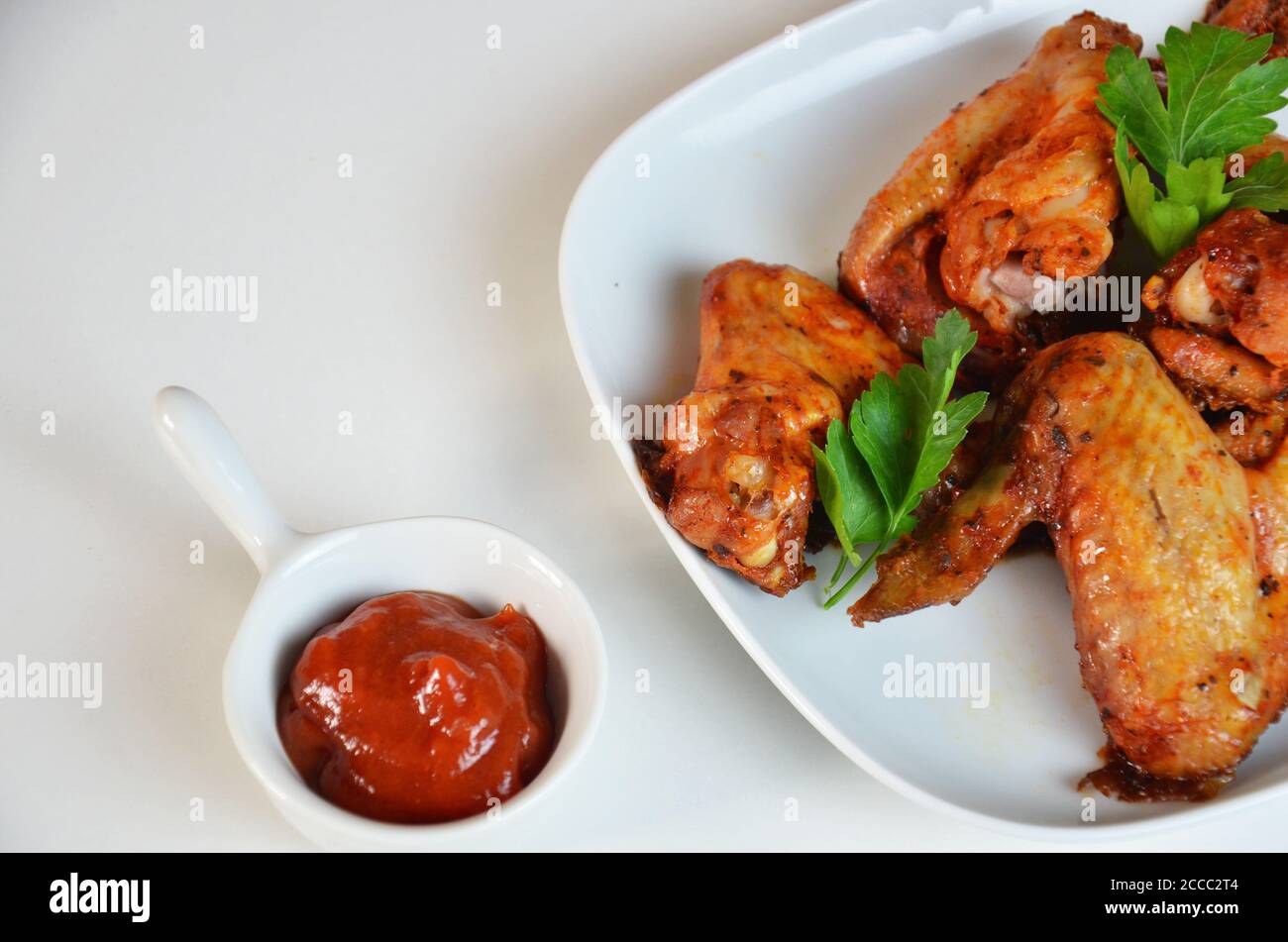 plate of chicken wings on white table red sauce in a gravy boat Stock Photo