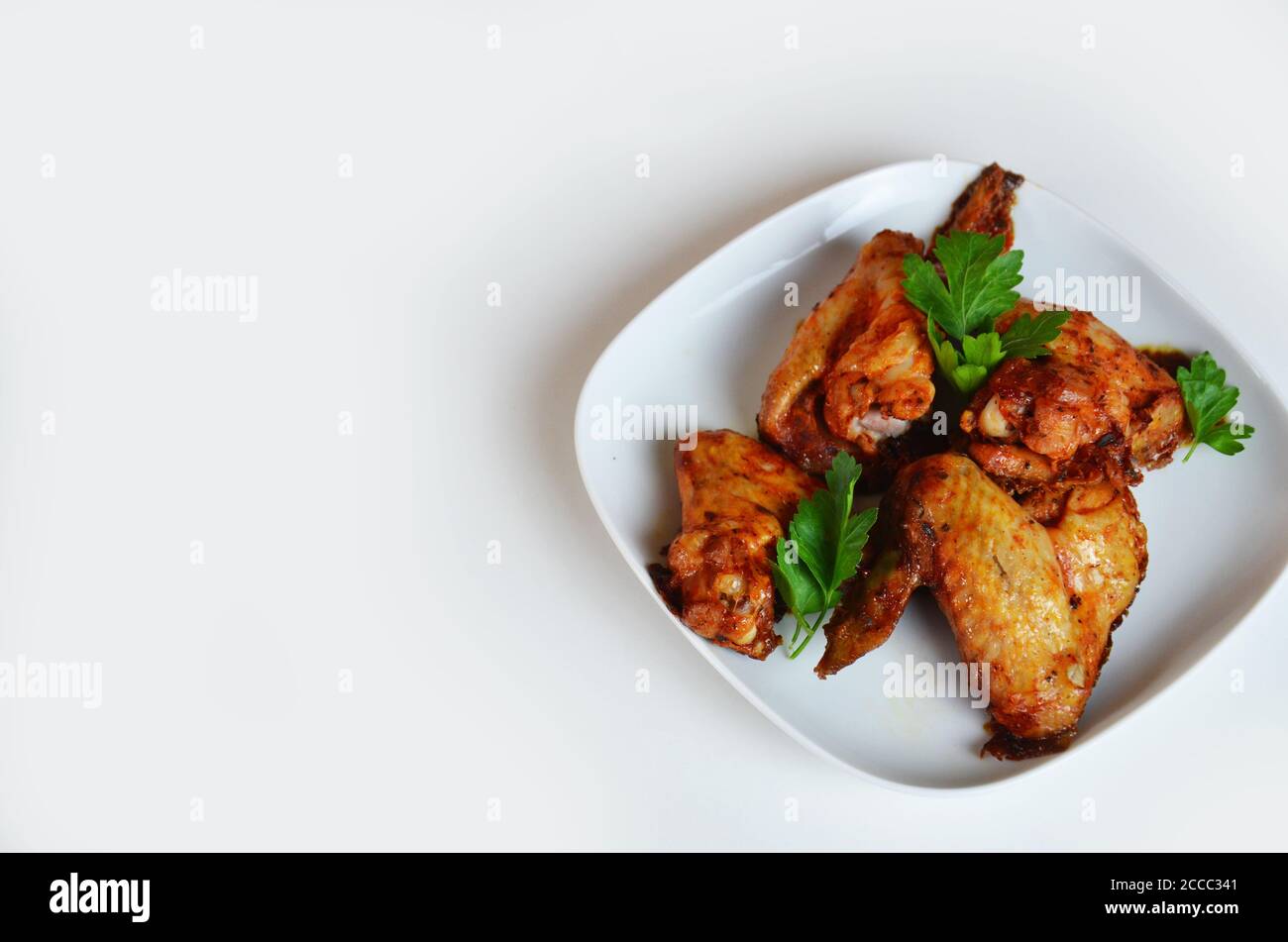 plate of chicken wings on white table red sauce in a gravy boat Stock Photo