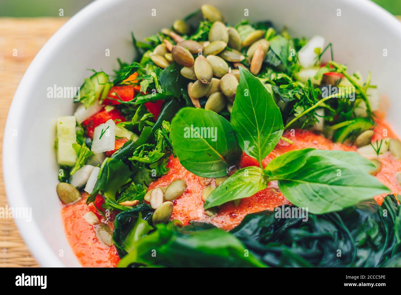 Beautiful raw vegan salad from green leaves mix vegetables in white plate. Cooking recipe Blended tomato carrot cauliflower, cut parsley cilantro dill Stock Photo