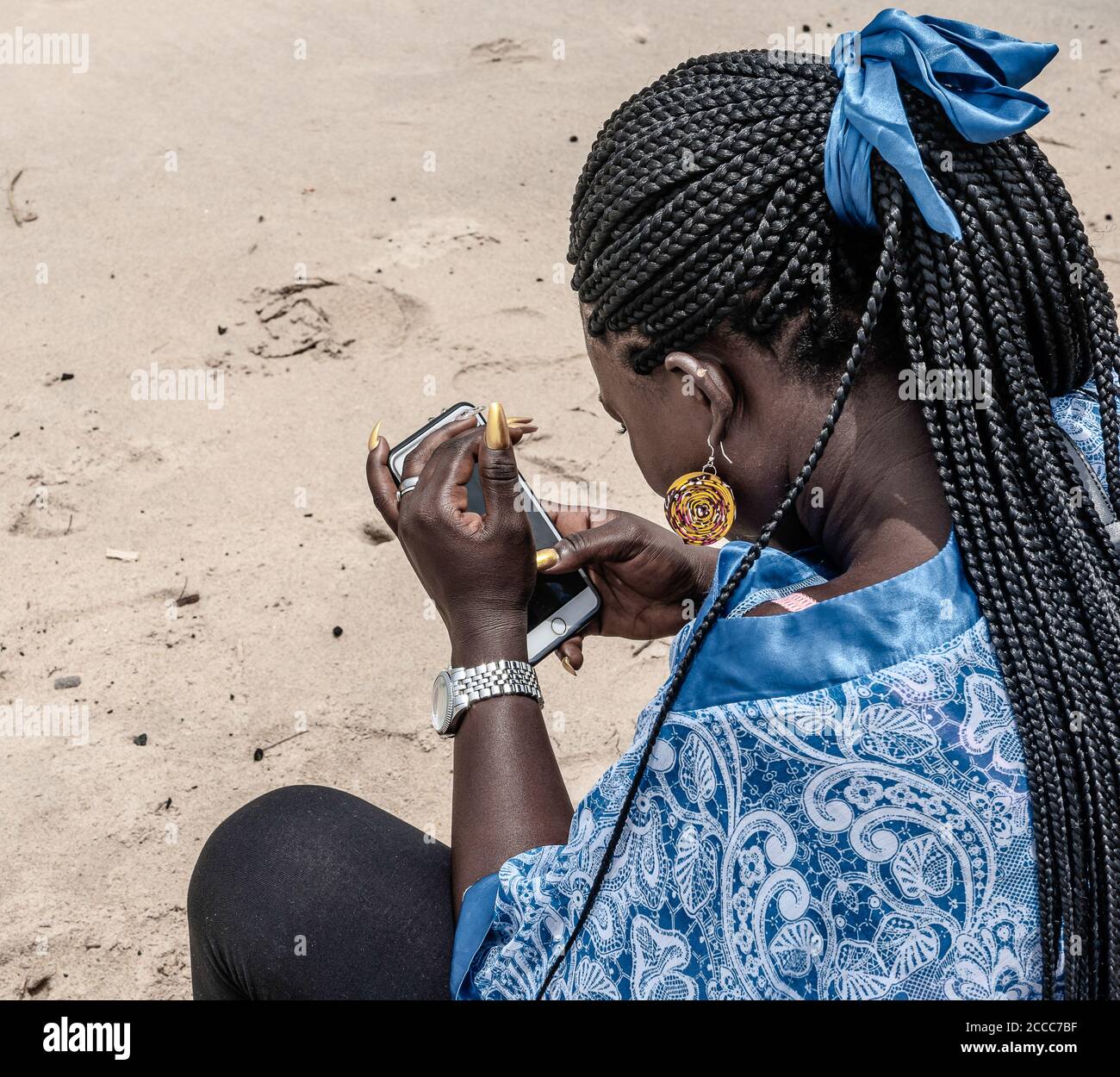 African woman holding a mobile phone in her hand and wearing traditional blue African dress sitting on the beach in the old fishing village of Shama i Stock Photo - Alamy African woman holding a mobile phone in her hand and wearing traditional blue African dress sitting on the beach in the old fishing village of Shama i Stock Photo - Alamy