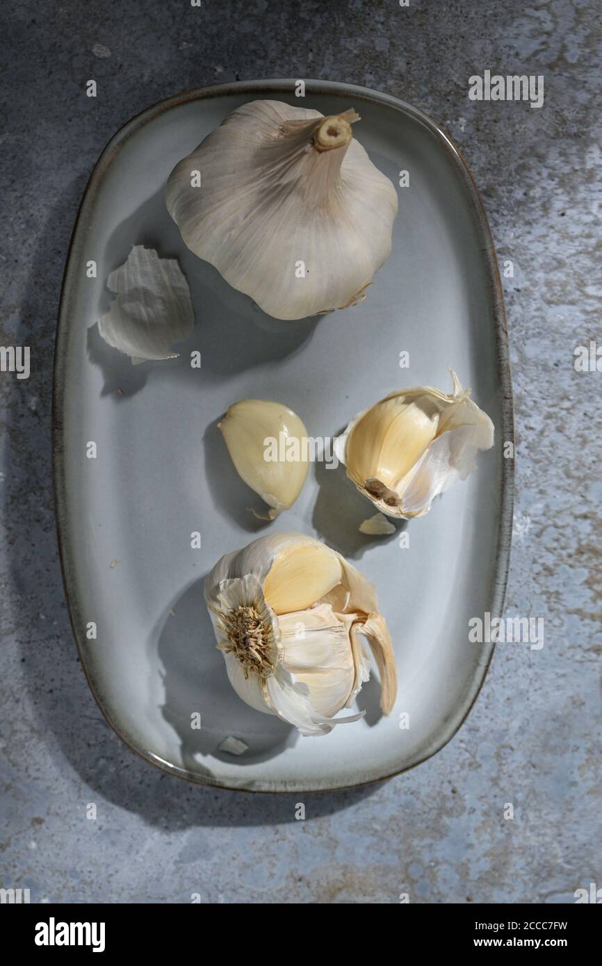 Garlic bulbs and cloves on a blue grey plate and a stone background, healthy food and medical plant, high angle view from above, selected focus, narro Stock Photo