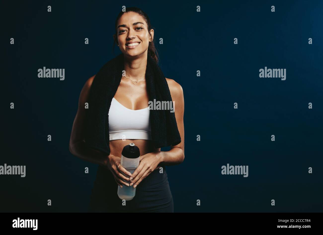 Fit woman taking break after workout holding a water bottle. Smiling ...