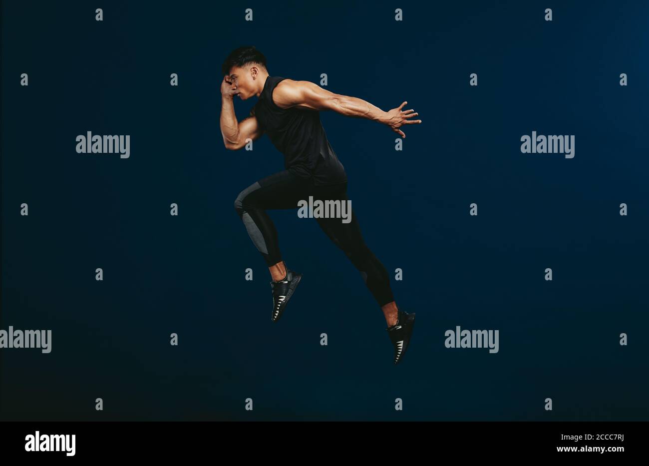 Sports man doing jumping and stretching workout. Full length of healthy fitness man doing exercise over dark background. Stock Photo