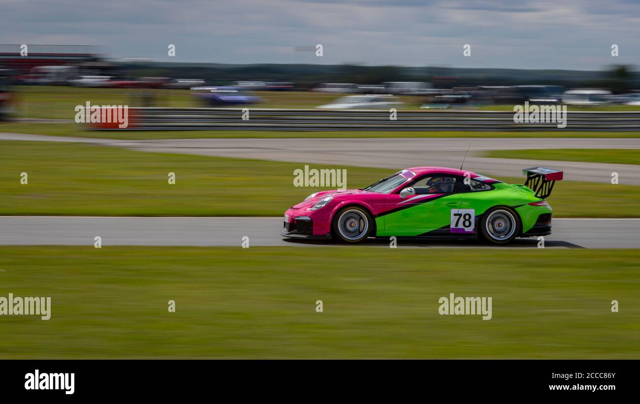 A panning shot of a pink and green racing car as it circuits a track