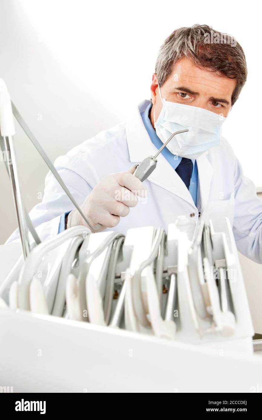 Dentist with face mask and aspirator in his practice Stock Photo