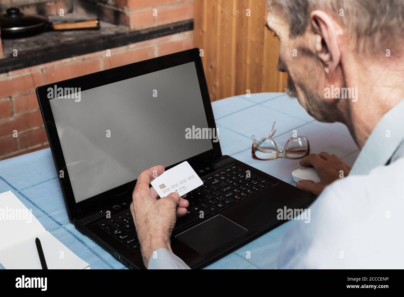 Senior man holding white credit card in front of laptop with blank screen for online shopping Stock Photo