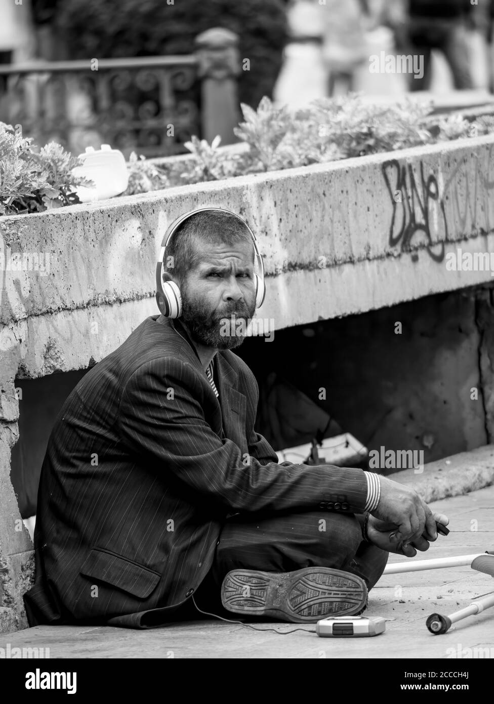 Bucharest/Romania - 07.25.2020: Homeless man or beggar sitting on the sidewalk and wearing headphones. Stock Photo