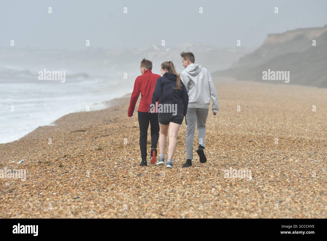 Teenagers on the beach in a storm at Milford-on-Sea, Hampshire, UK, August 2020. Weather: Storm Ellen battering the south coast of England at the height of the summer holiday season with wind gusts of up to 60 mph and a high tide. Stock Photo