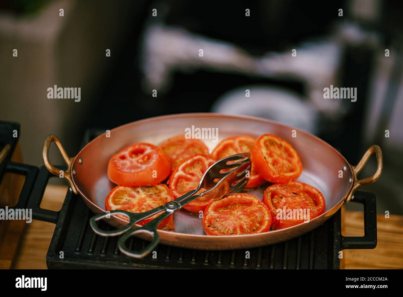 Closeup of sliced fried tomatoes in a frying pan on a cast iron stove
