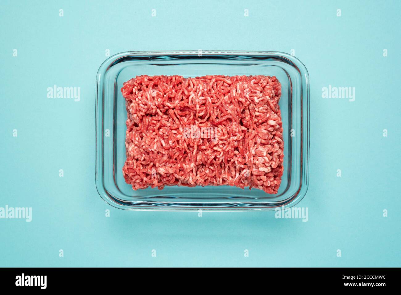 Above view with ground beef in a glass food container on a blue colored table. Ground beef in a glass dish isolated on a blue background. Stock Photo