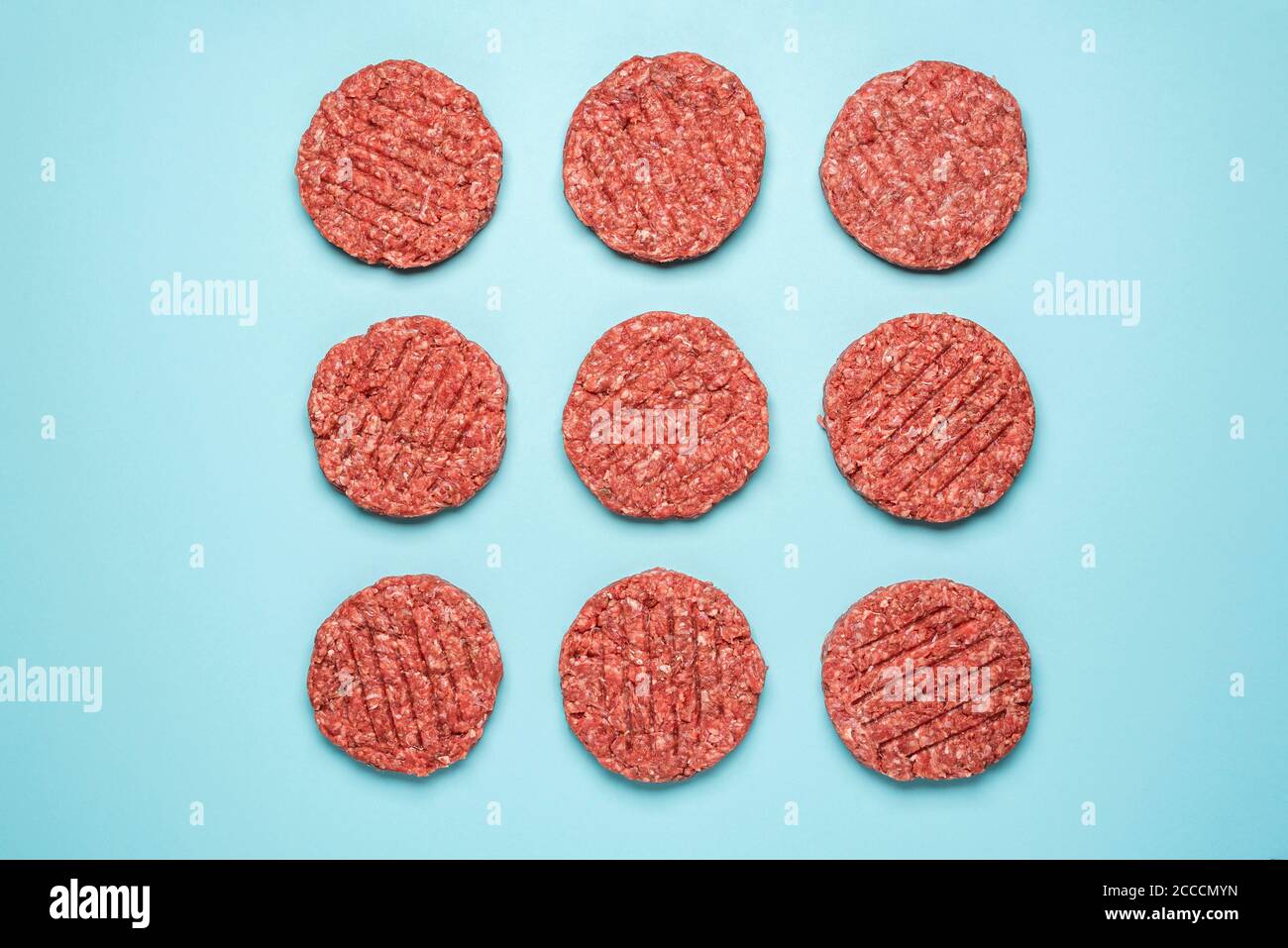 Above view with raw beef patties for burgers,  arranged symmetrically on a blue colored background. Flat lay with nine uncooked burger patties isolate Stock Photo