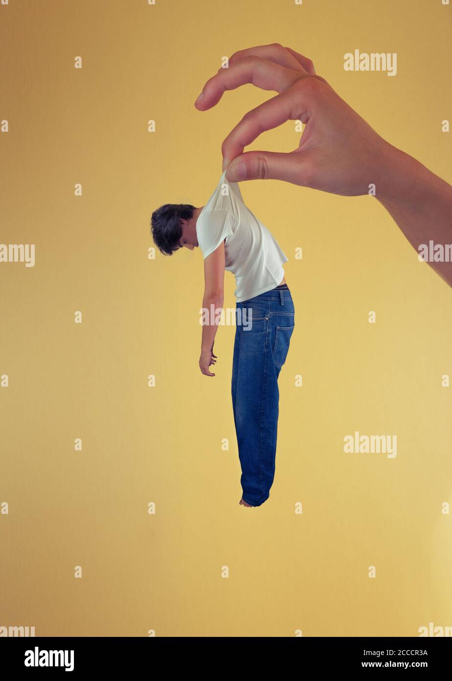 Inconscious young man being grabbed by the t-shirt by a giant hand like it is about to drop him Stock Photo