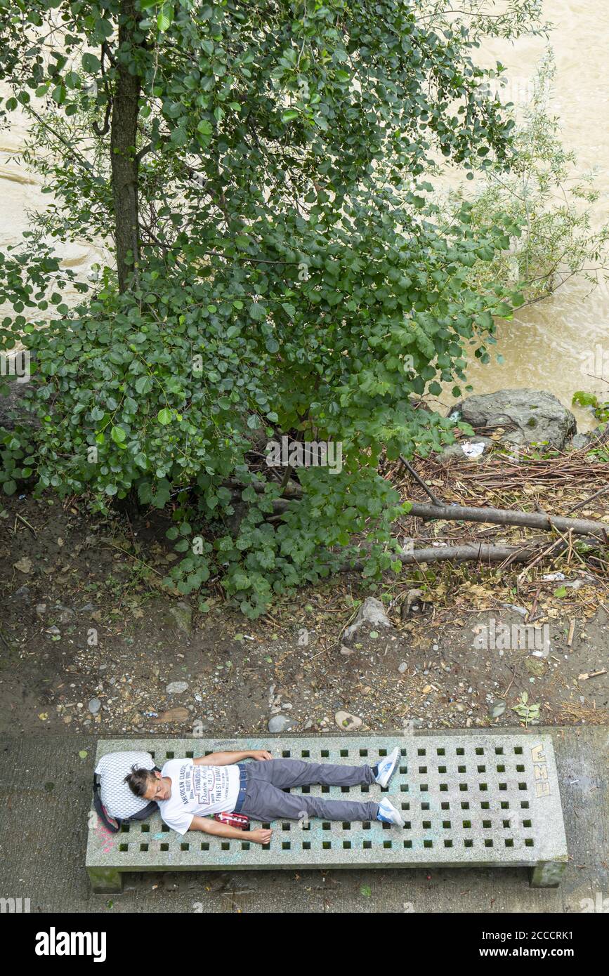 Graz, Austria. August 2020.  a tired young man rests lying on a bench on the Mur riverfront Stock Photo