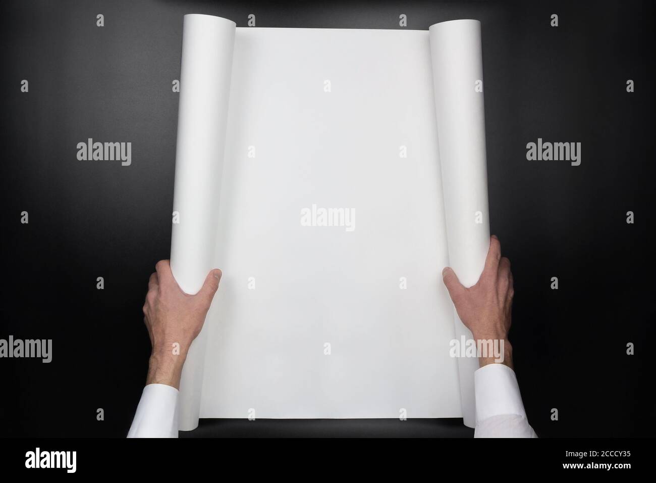 Man's hands hold blank paper scroll on black background, top view Stock Photo