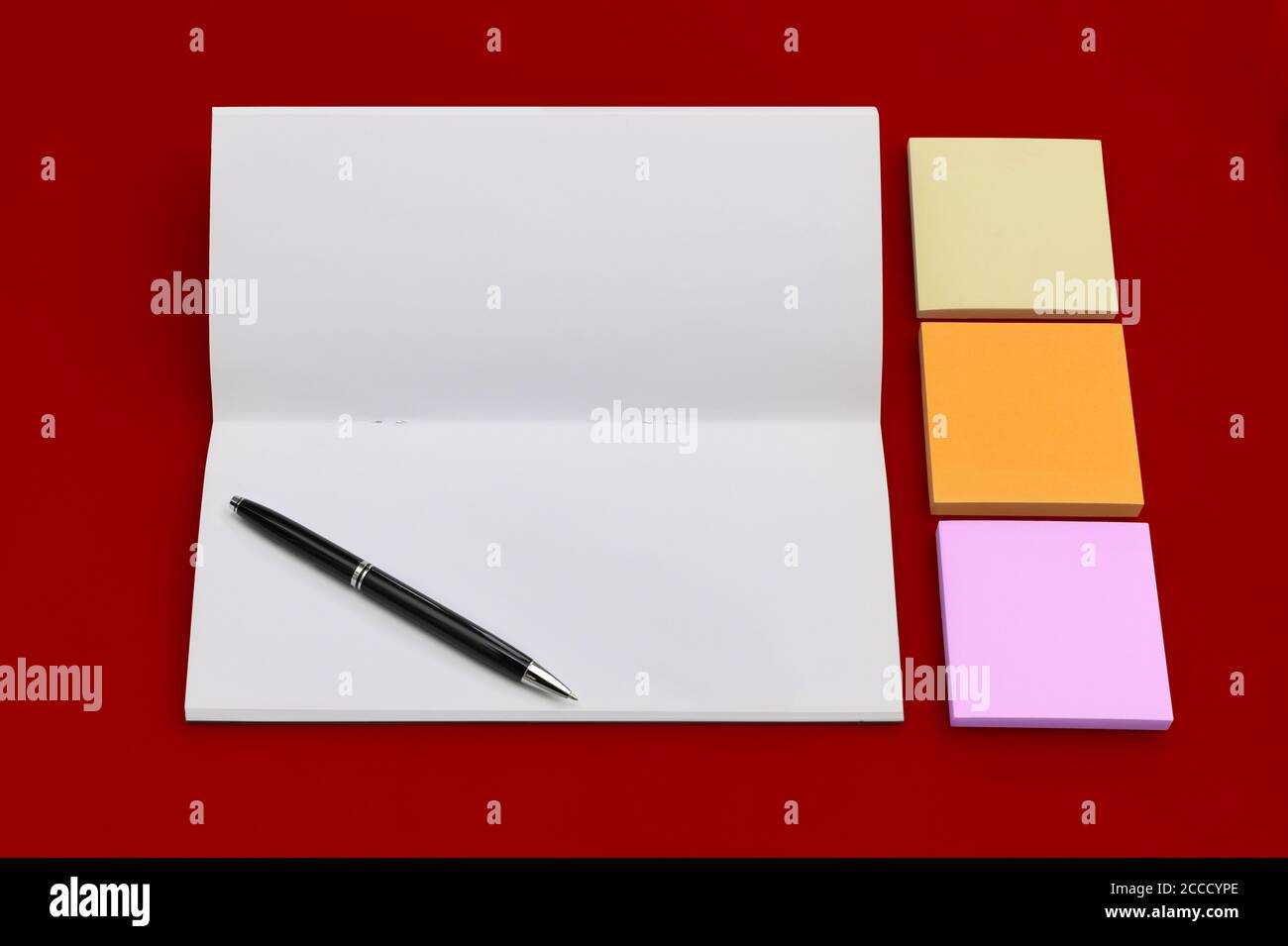 Business copy space with notebook, pen and multicolored sticky notes on red background Stock Photo