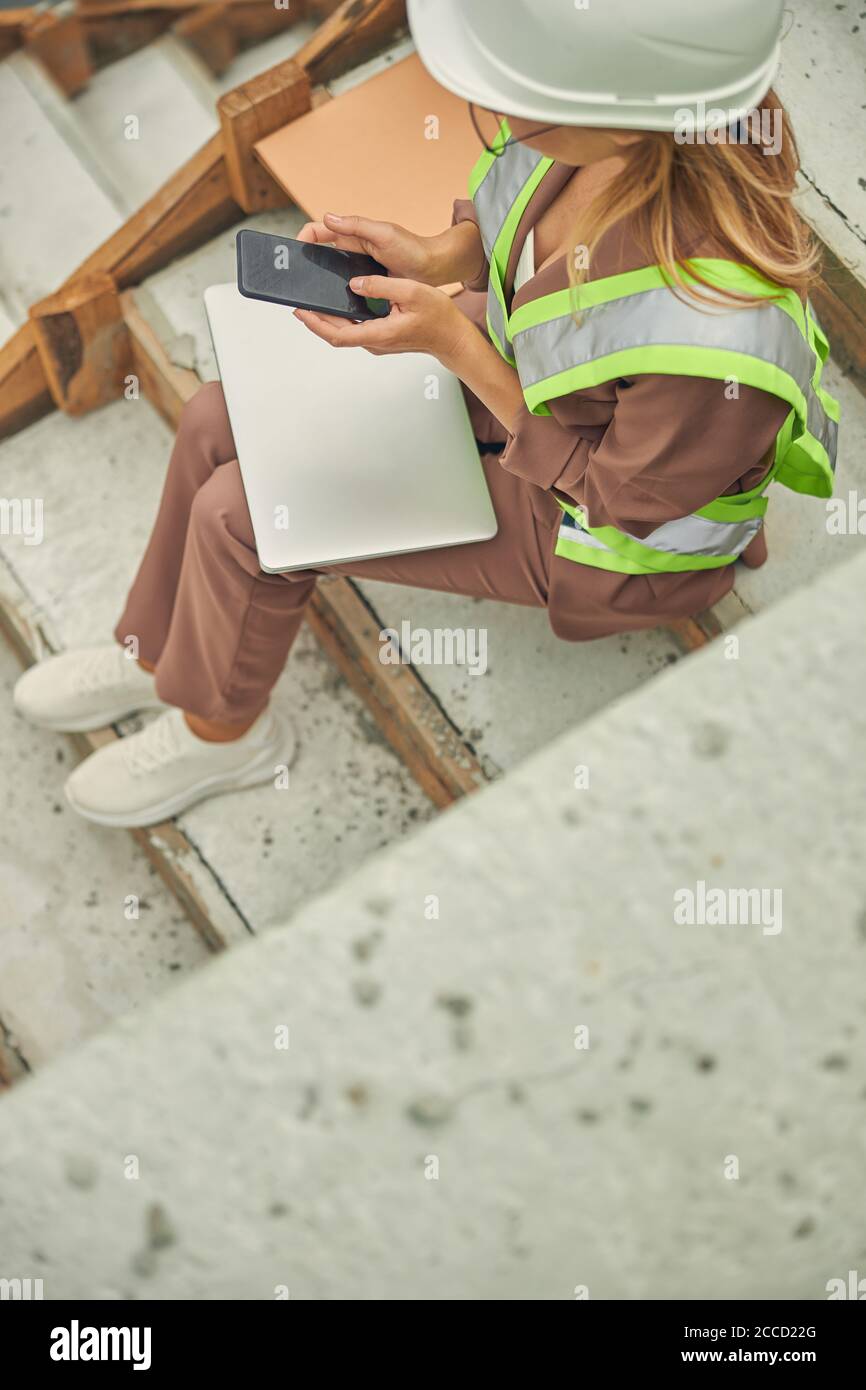 Woman in a hard hat using her smartphone Stock Photo