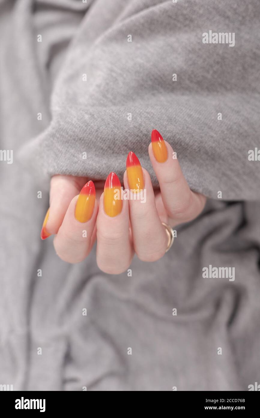Female hand with long nails and yellow, orange and red gradient manicure  holds a bottle of nail polish Stock Photo - Alamy