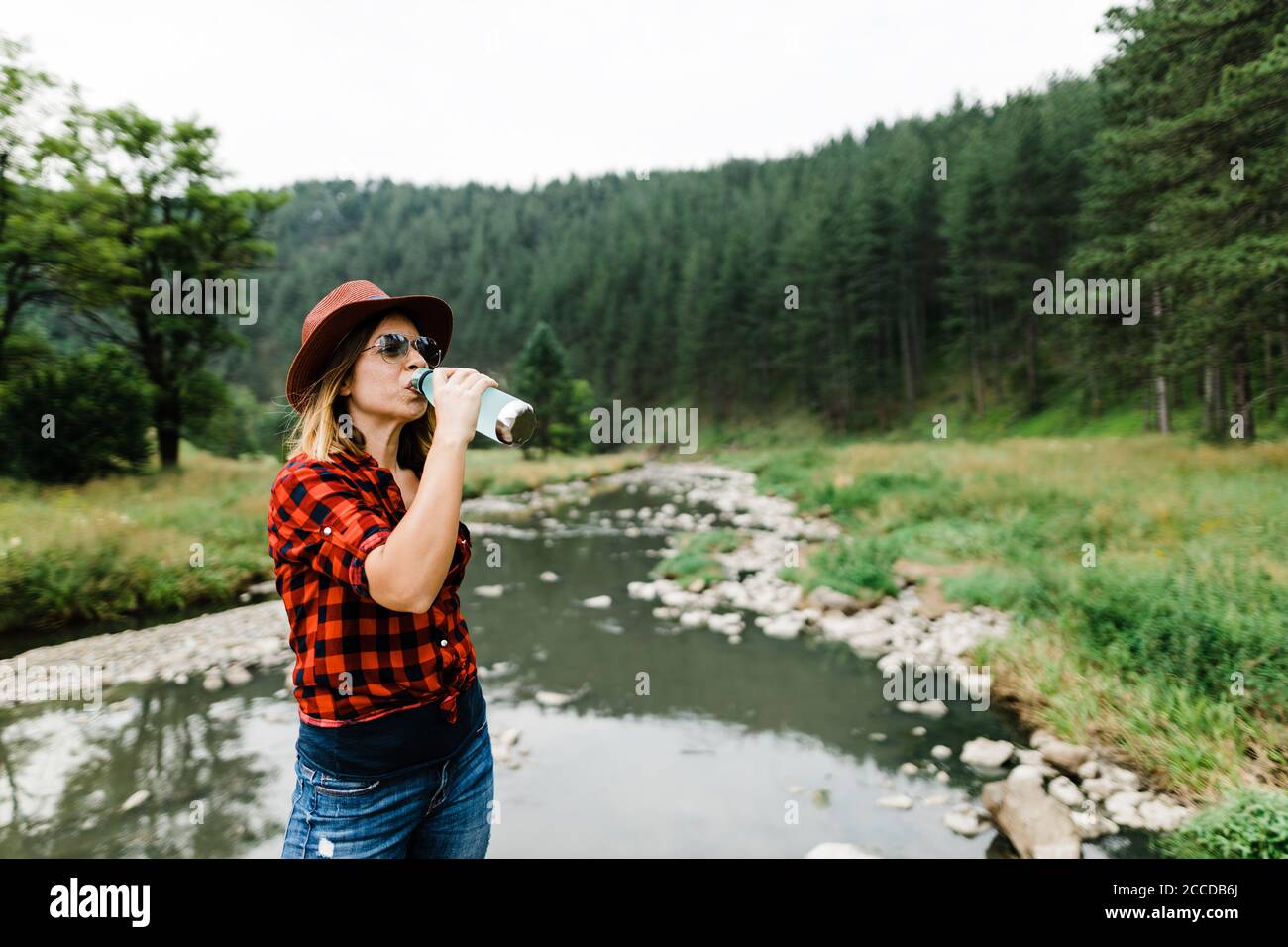 Young female nature lover drinking water from the bottle by the river Stock Photo