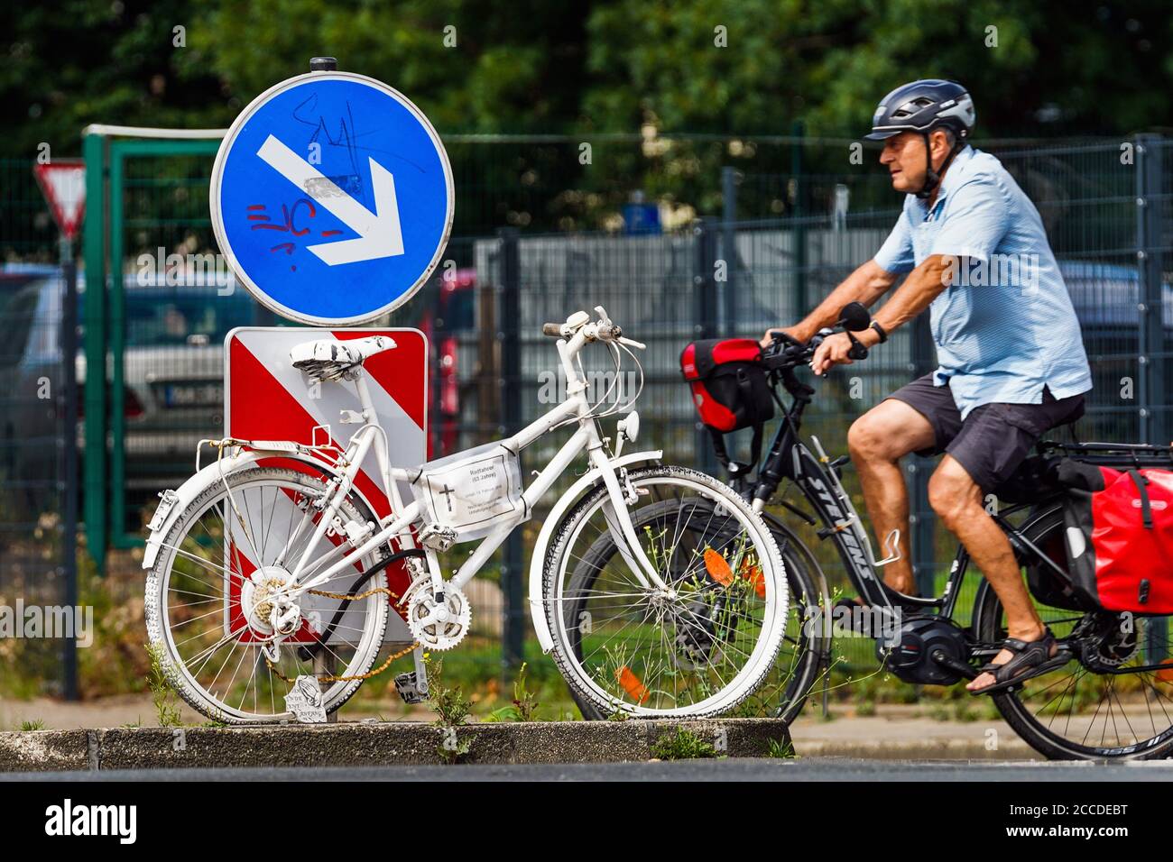Dortmund, 21.08.2020: Radfahrer passiert ein weisses Fahrrad, Geisterfahrrad. Es erinnert an einen Radfahrer, der 2018 an einer Straßenkreuzung in Dortmund nach einem Verkersunfall tödlich verunglückt ist.   ---   Dortmund, 08/21/2020: Cyclist passes a white bike, ghost bike. It is commemorates of a cyclist who died in a road junction in Dortmund in 2018 after a traffic accident. Stock Photo