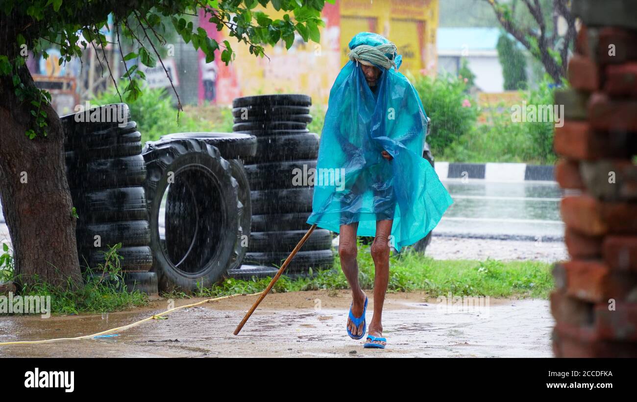 An Indian old man walking in the pouring rain in the small village. Stock Photo