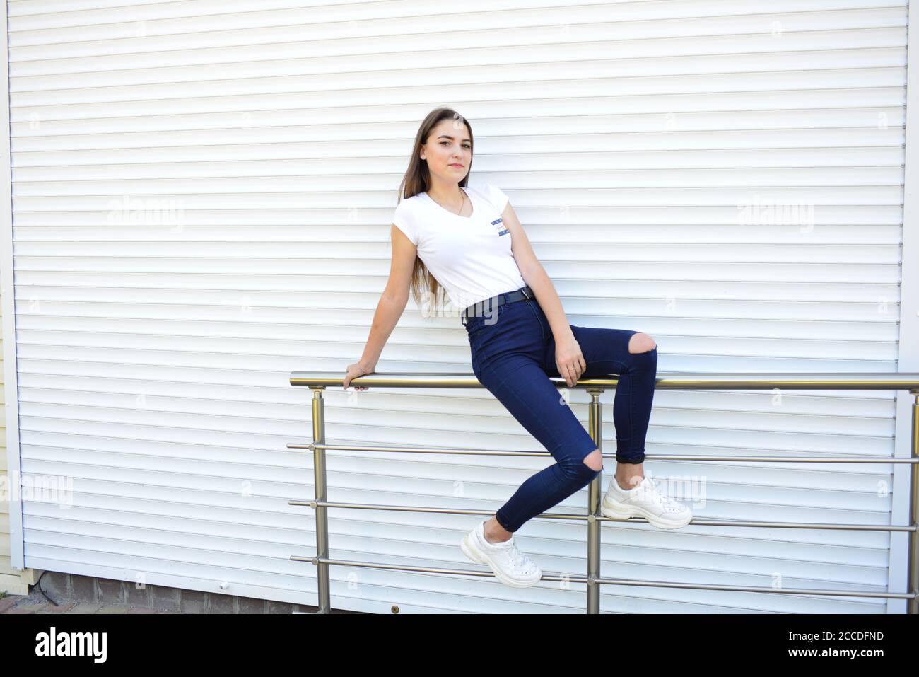 Beautiful young woman wearing jeans, white t-shirt, standing on the street. photo near iron fence Stock Photo