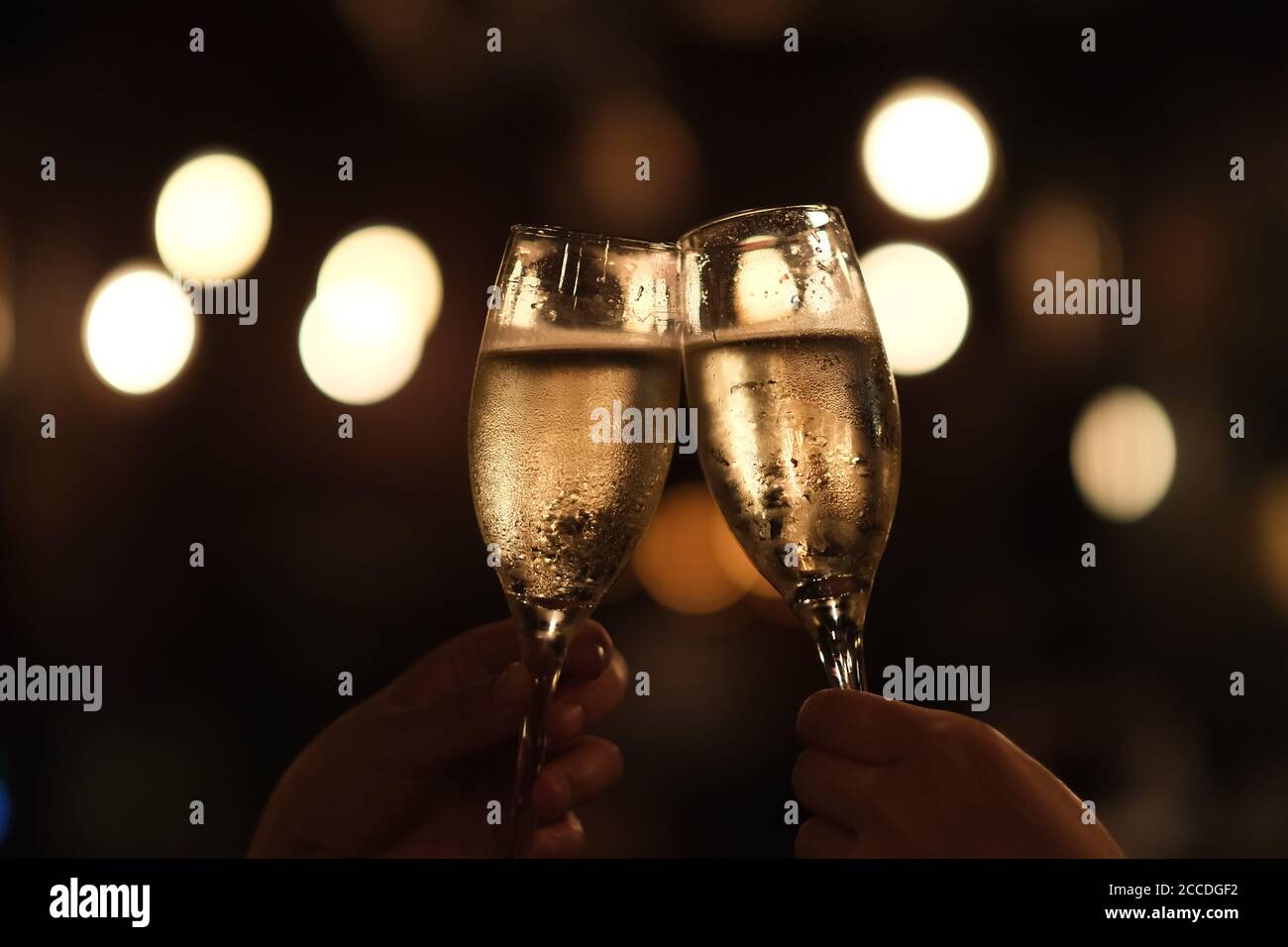close up two hands holding drinking glass, cheers in darkness. Golden bokeh background Stock Photo