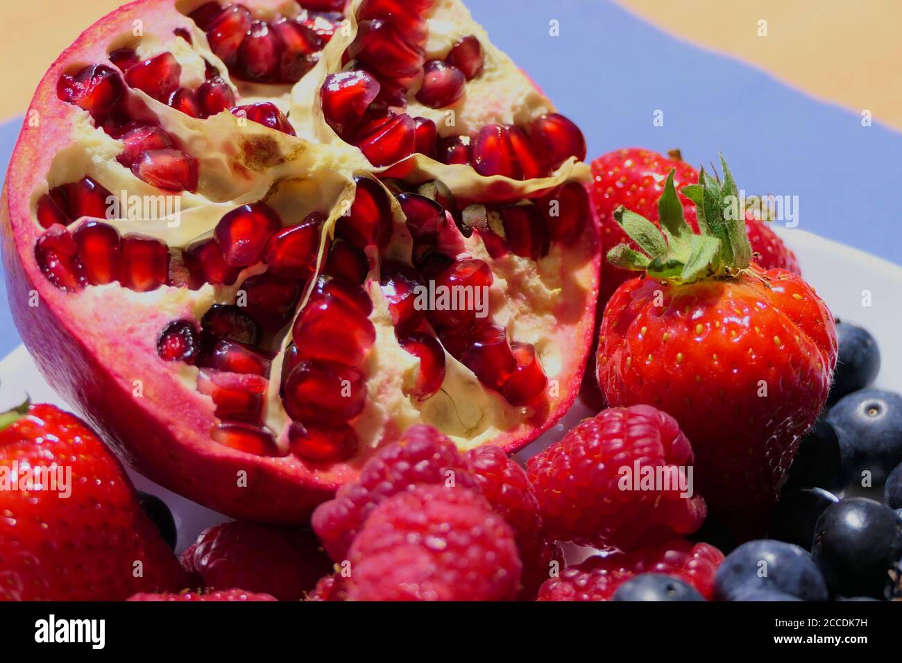 Macro shot of a fresh sliced sunlit pomegranate and mixed berries Stock Photo