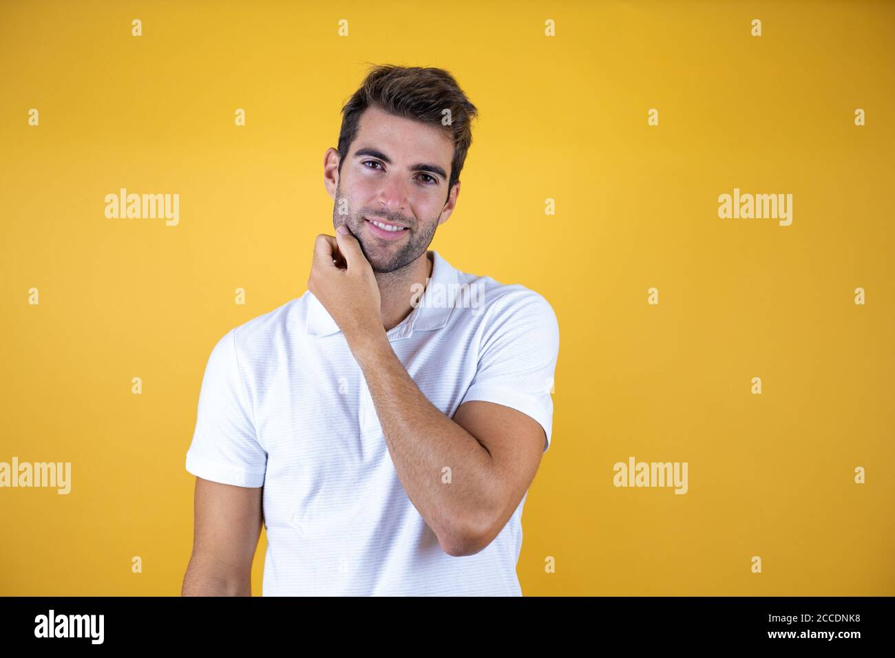 Young handsome man over yellow background touching beard looking at the camera Stock Photo
