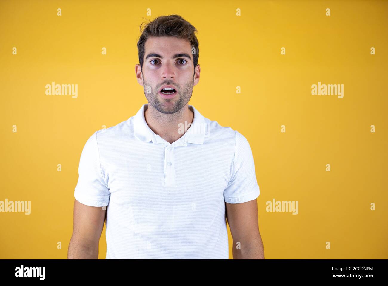 Young handsome man standing over insolated yellow background surprised and amazed Stock Photo