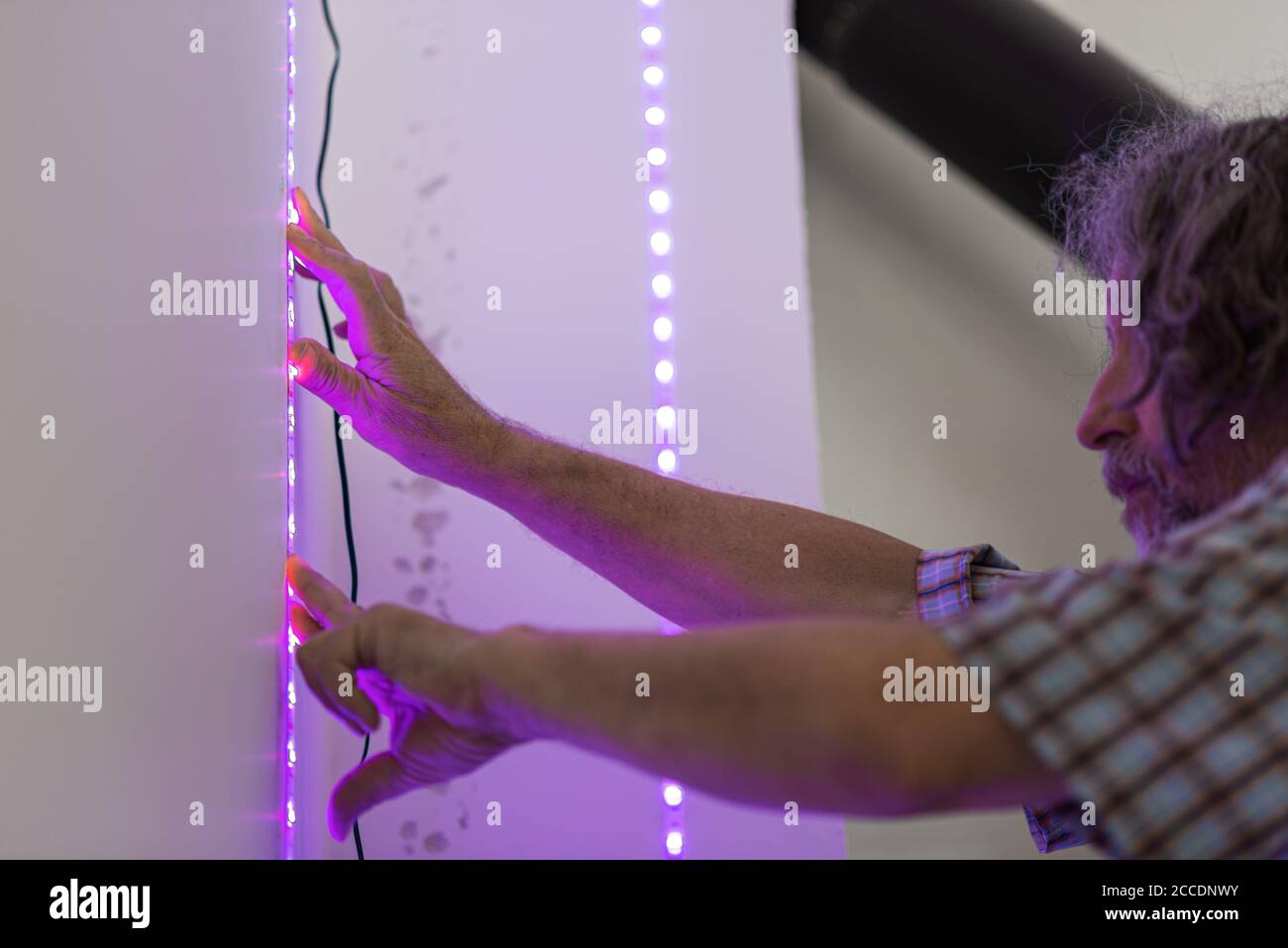 Senior male electrician placing decorative led lights stripe  on a wall. Stock Photo