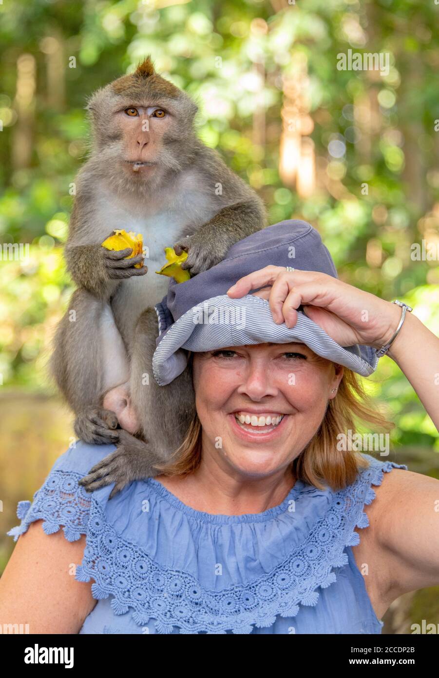 Vertical portrait of a female tourist with a macaque sitting on her shoulder in Bali. Stock Photo